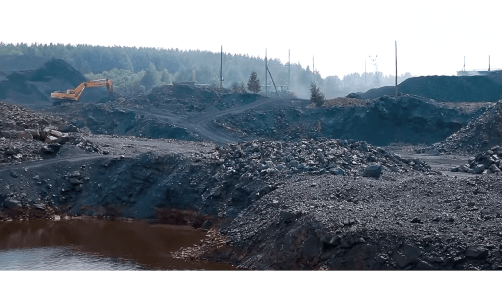 Excavation site of a Shungite mine, featuring large piles of dark materials and heavy machinery in the background.