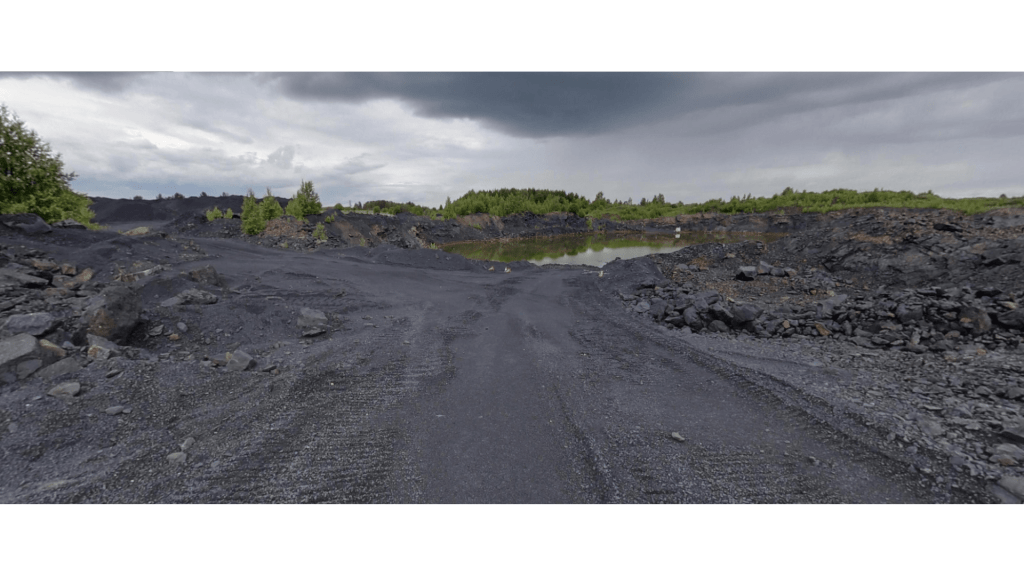A view of an active shungite mine in Karelia, Russia, featuring rocky terrain and patches of greenery under a cloudy sky.