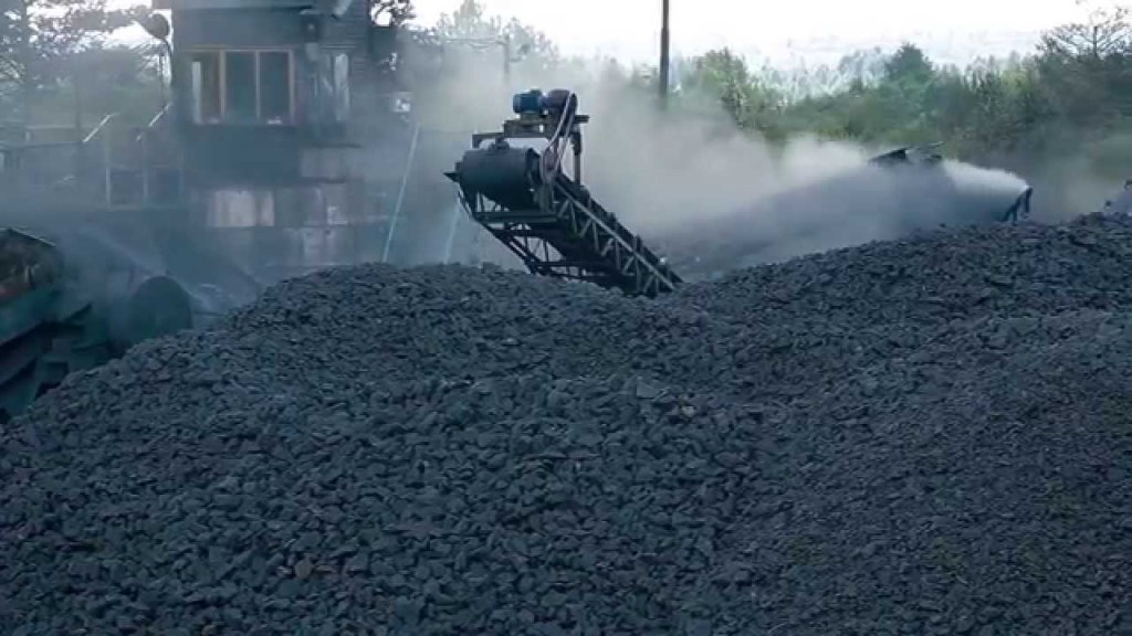 A mining site with a conveyor belt transporting shungite stone, surrounded by mounds of dark mineral deposits and machinery under a cloudy sky.