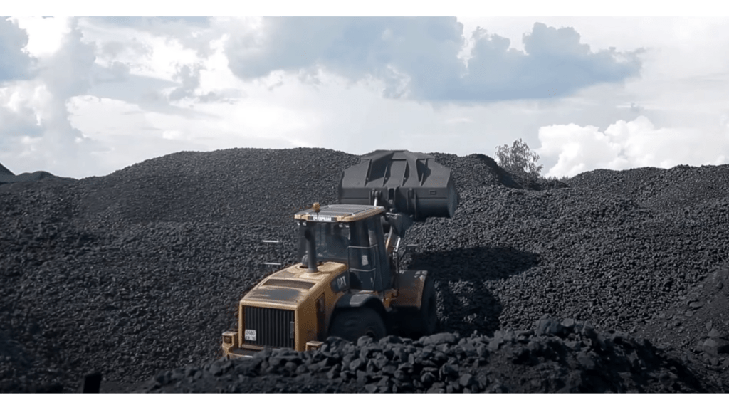 A large yellow loader machinery working on a mound of black material at a mining site under a cloudy sky.