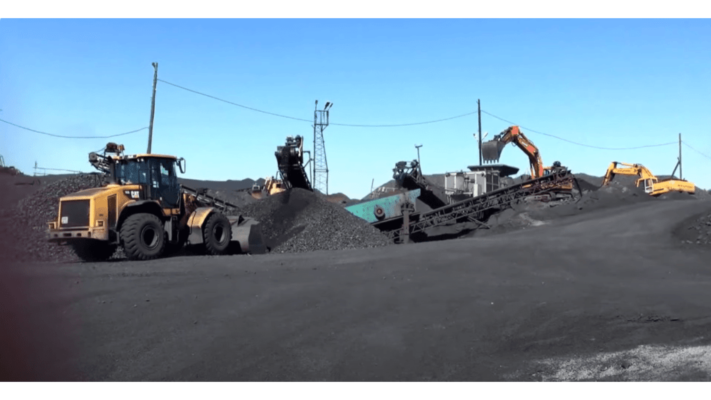 Heavy machinery operating at a shungite mining site with piles of black material and clear blue sky.